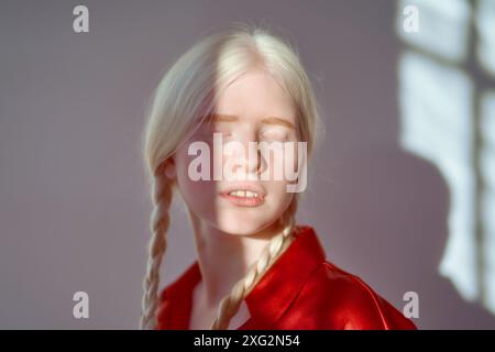 Foto estetica di una ragazza albino inclusiva illuminata dalla luce del sole su sfondo bianco. Foto Stock