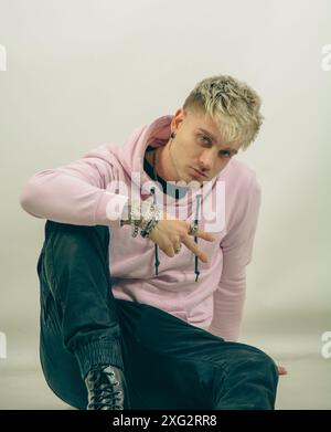 Un uomo che indossa una felpa con cappuccio rosa sta facendo il segno V per la vittoria con la sua mano. Il suo braccio è esteso, e sembra che stia dirigendo l'attenzione verso un oggetto o direzione specifici. Foto Stock