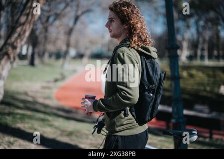 Giovane con i capelli ricci che tiene una tazza di caffè accanto a una bicicletta in un parco soleggiato Foto Stock