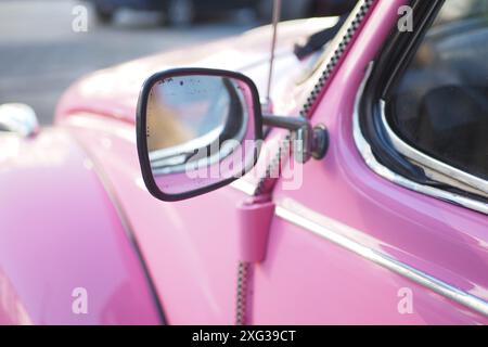 Foto ravvicinata di uno specchio laterale di auto rosa d'epoca su un veicolo classico sotto il sole Foto Stock