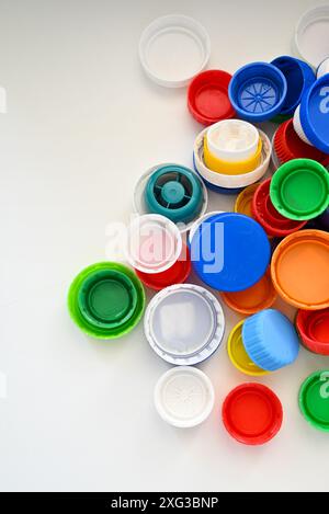 I tappi in plastica multicolore di diverse dimensioni e forme dei flaconi in plastica sono sparsi su un tavolo in legno bianco Foto Stock