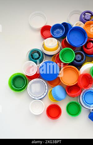 I tappi in plastica multicolore di diverse dimensioni e forme da bottiglie in plastica sono sparsi su un tavolo di legno bianco in pile Foto Stock