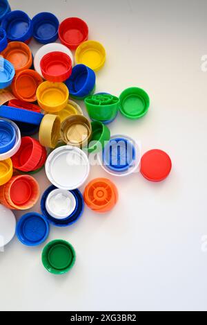 I tappi in plastica multicolore di diverse dimensioni da bottiglie in plastica sono sparsi su un tavolo di legno bianco in pile Foto Stock