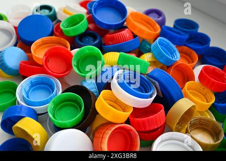 I tappi in plastica multicolore di diverse dimensioni dei flaconi in plastica sono sparsi su un tavolo bianco in pila Foto Stock