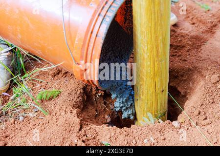 Versamento di calcestruzzo su pali di recinzione in legno recentemente installati Foto Stock