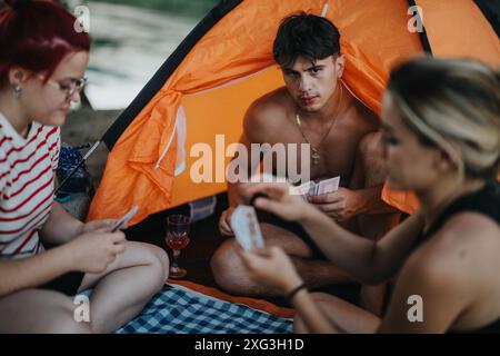 Amici che si godono un picnic in campeggio giocando insieme a giochi di carte nella natura Foto Stock