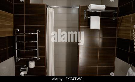Bagno in una camera d'albergo. Asciugamano bianco nel bagno dell'hotel. Asciugamani bianchi vicino a piastrelle di ceramica marrone. Foto Stock