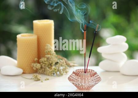 Bastoncini di incenso che si mescolano nel supporto vicino a pietre, candele e fiori secchi su un tavolo di legno all'aperto Foto Stock