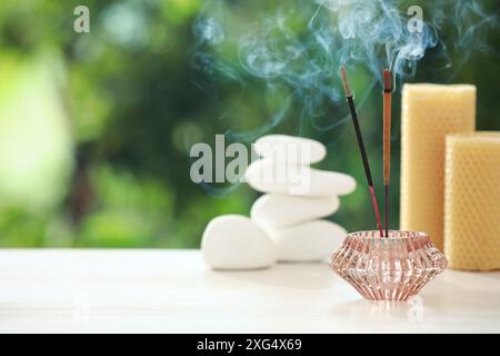 Bastoncini di incenso che si fondono nel supporto vicino a pietre e candele su tavoli di legno all'aperto, spazio per il testo Foto Stock