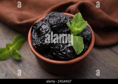 Gustose prugne secche (prugne) e menta nel recipiente su un tavolo di legno, primo piano Foto Stock