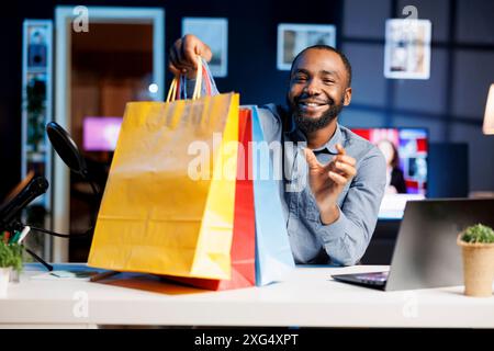 Uomo afroamericano che filma vlog di moda, diboxe borse con ordine via Internet, mostrando agli abbonati acquisti che ha recentemente ottenuto. Influencer che presenta agli spettatori nuove acquisizioni di acquisti Foto Stock