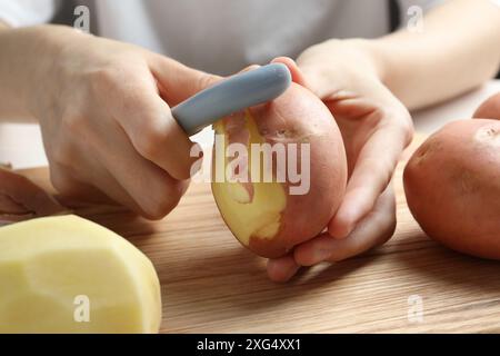 Donna che sbuccia patate fresche con pelapatate a tavola, primo piano Foto Stock