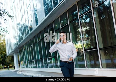 Un uomo che indossa una camicia bianca e pantaloni blu è impegnato in una conversazione telefonica. Foto Stock