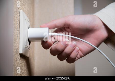 Primo piano della mano di una donna che inserisce un caricabatterie usb bianco in una presa da 220 volt Foto Stock