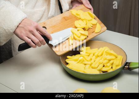 Il concetto di tagliare e cucinare le patate. Le mani di una giovane donna in un abito da vestire, con un coltello in mano e un tagliere di legno, sopra Foto Stock