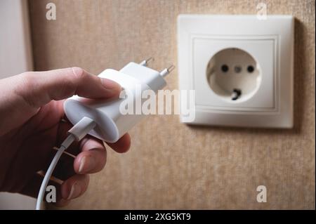 La mano si accende, spegne il caricabatterie nella presa elettrica a muro. Caricabatterie bianco per telefono in primo piano con la mano di una donna Foto Stock