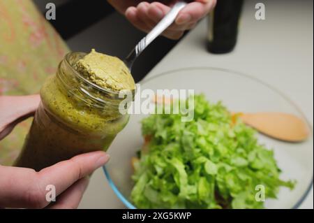 Primo piano delle mani di una cuoca che mette la salsa in un piatto di verdure, sta preparando un piatto per la sua famiglia in cucina Foto Stock