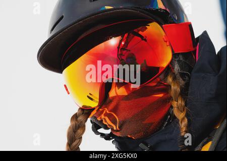 Ritratto di una giovane donna sana in maschera sportiva e casco che trascorre le vacanze invernali sulle montagne innevate. La ragazza prende un ascensore e guarda il Foto Stock