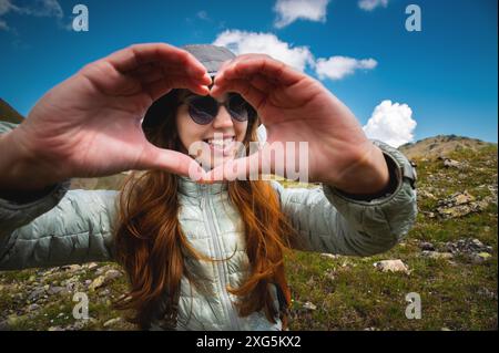 Mani a forma di cuore d'amore. Una giovane donna fa un cuore con le mani. Ragazza turistica in cima alla montagna con uno zaino, il concetto Foto Stock