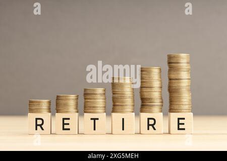 Ritira la parola in blocchi di legno con monete impilate in pile crescenti. Ritirarsi nel concetto di ricchezza. Spazio di copia Foto Stock