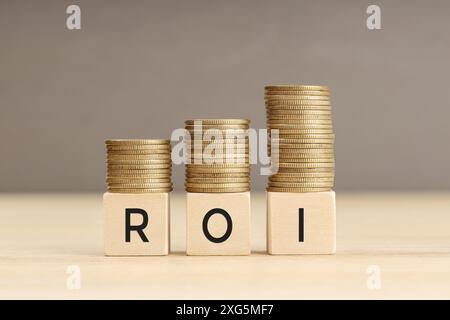 Parola di ROI in blocchi di legno con monete impilate in pile crescenti. Concetto di ritorno sull'investimento. Spazio di copia Foto Stock