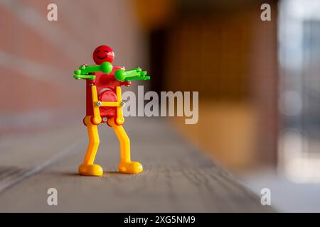 Foto di un divertente robot giocattolo di plastica che fa una felice danza, festeggia, su una superficie di legno. Foto Stock