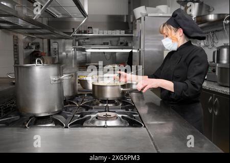 Gruppo di chef che cucinano insieme in cucina al ristorante indossando maschera medica protettiva in coronavirus nuovo concetto normale. Foto di alta qualità Foto Stock