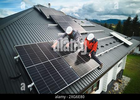 Tecnici professionisti che assicurano pannelli fotovoltaici solari pesanti. Lavoratori maschi che installano una batteria solare su un tetto. Concetto di risorse ecologiche. Foto Stock