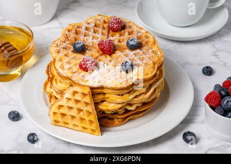 Una pila di waffle belgi con i frutti di bosco. Deliziosa colazione estiva dall'alto. Waffle a forma di cuore e mix di lamponi e mirtilli come Foto Stock