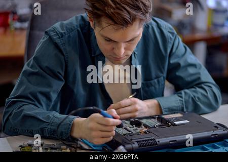 uomo caucasico che ripara parti in un computer portatile rotto smontato utilizzando un cacciavite e diversi utensili sul tavolo in officina, un tecnico professionista presso il wor Foto Stock