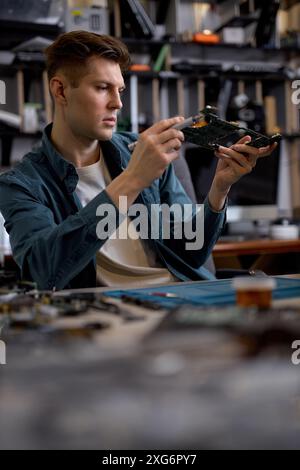 Un tecnico o un riparatore qualificato ripristina il PC portatile esaminando i dettagli delle parti del computer portatile smontato. Officina di riparazione elettronica, tec Foto Stock