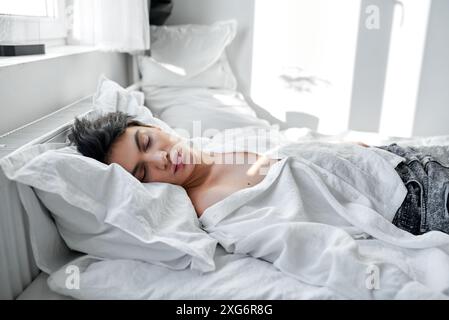 Vista dall'alto di un bel giovane ragazzo con t-shirt bianca che riposa a casa, dorme da solo nel suo comodo letto king size, concetto di sonno sano, morto ragazzo i Foto Stock
