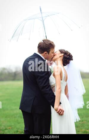 sposi e sposi in un giorno di nozze piovoso che cammina sotto un ombrello Foto Stock