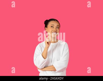 Giovane donna che pensa e punta verso l'alto sullo sfondo rosa Foto Stock