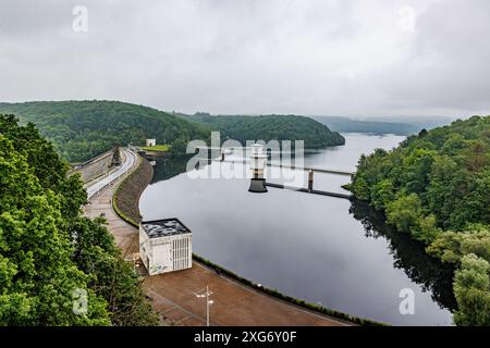 Vista aerea della diga di Gileppe, parete con sentiero pedonale sulla cresta, due torri di aspirazione o uscita che sporgono dalle acque del lago, alberi lussureggianti nella montagna della valle Foto Stock