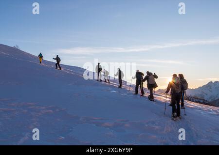 il gruppo di racchette da neve si trova di fronte alla salita sul versante innevato della montagna Foto Stock