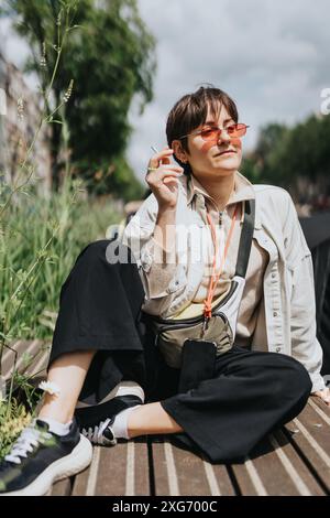 Giovane donna che si rilassa all'aperto indossando eleganti occhiali da sole e un outfit casual Foto Stock