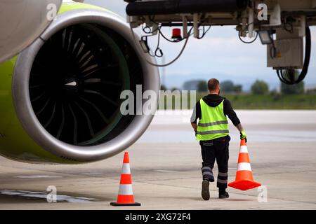 Il lavoratore dell'aeroporto sposta i coni vicino a un aereo su una pista. Foto Stock