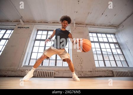 Action shot grandangolare del giocatore di basket afroamericano che dribbling ball mentre si pratica in palestra coperta Foto Stock