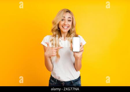 Donna sorridente che tiene lo smartphone davanti allo sfondo giallo, Mockup Foto Stock