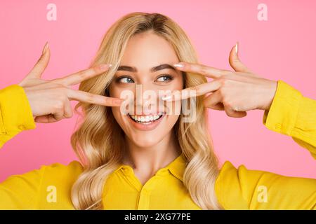 La donna bionda sorride con segni di pace davanti agli occhi Foto Stock