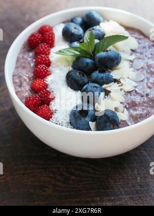 Ciotola per frullato di mirtilli con semi di chia vegan fatta in casa con scaglie di cocco, mandorle e wineberries giapponesi Foto Stock