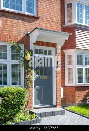 Vista frontale esterna della casa residenziale edoardiana in mattoni rossi nel sobborgo nord di Londra, con porta dipinta di grigio, baldacchino in legno e rose da arrampicata gialle. Foto Stock