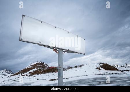 Un cartellone vuoto si erge su montagne innevate, un luogo ideale per testo o annunci pubblicitari con lo sfondo panoramico Foto Stock