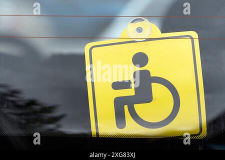 Primo piano di un permesso di parcheggio giallo accessibile con sedia a rotelle sul finestrino del veicolo che indica i diritti di parcheggio speciali Foto Stock