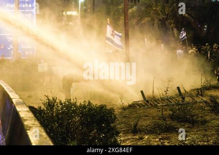 Tel Aviv, Israele. 6 luglio 2024. Il cannone d'acqua della polizia israeliana spruzza contro i manifestanti con una bandiera israeliana e un nastro giallo lungo l'autostrada Ayalon durante la dimostrazione. Oltre 100.000 israeliani hanno manifestato a Kaplan con le famiglie degli ostaggi contro il primo ministro Benjamin Netanyahu, chiedendo un accordo immediato con gli ostaggi e il cessate il fuoco, durante la manifestazione, i manifestanti hanno bloccato l'autostrada Ayalon e sono stati dispersi da un cannone d'acqua della polizia. Credito: SOPA Images Limited/Alamy Live News Foto Stock