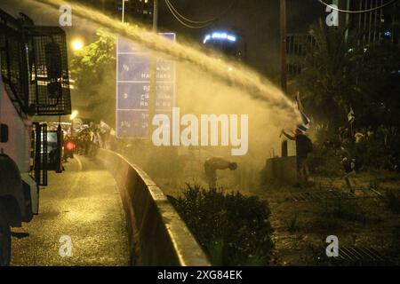 Tel Aviv, Israele. 6 luglio 2024. Il cannone d'acqua della polizia israeliana spruzza contro un manifestante con una bandiera israeliana lungo l'autostrada Ayalon durante la manifestazione. Oltre 100.000 israeliani hanno manifestato a Kaplan con le famiglie degli ostaggi contro il primo ministro Benjamin Netanyahu, chiedendo un accordo immediato con gli ostaggi e il cessate il fuoco, durante la manifestazione, i manifestanti hanno bloccato l'autostrada Ayalon e sono stati dispersi da un cannone d'acqua della polizia. Credito: SOPA Images Limited/Alamy Live News Foto Stock