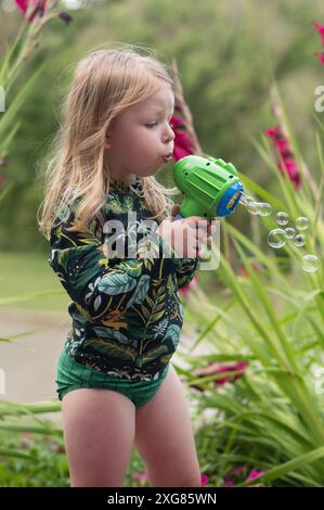 Bambina di tre anni con lunghe bolle bionde che soffiano Foto Stock
