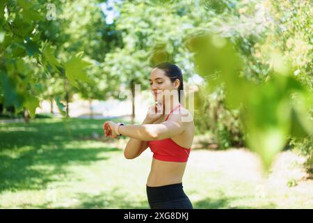 Una donna si allena nel parco, controllando il suo fitness tracker, dedicato a rimanere in salute in una giornata di sole Foto Stock