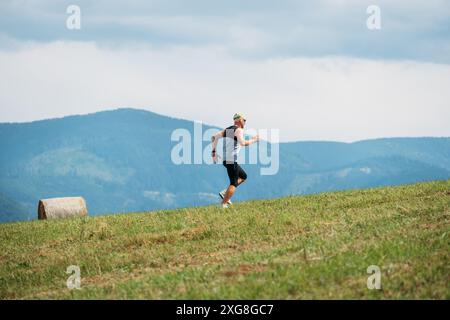 l'uomo corre in salita su una collina erbosa con montagne panoramiche sullo sfondo che incarnano lo spirito del trail running e dell'allenamento ultramaratona. Orizzontale Crea insp Foto Stock